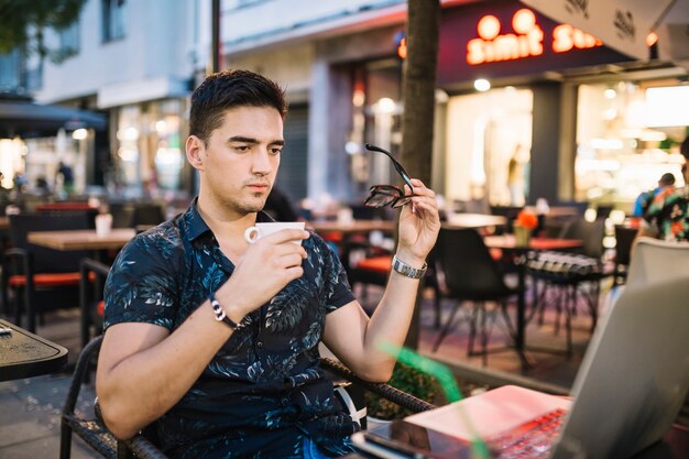 Bemannen Sie das Halten des Tasse Kaffees, der Laptop in cafÃ betrachtet