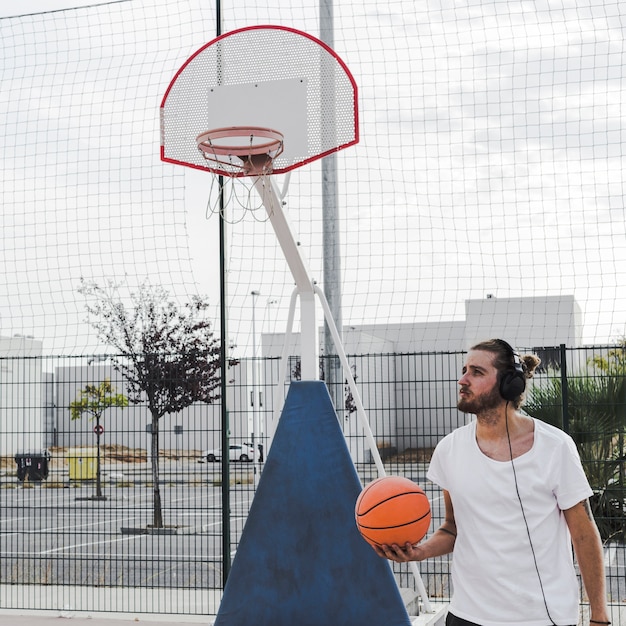 Bemannen Sie das Hören Musik auf dem Kopfhörer, der vor Gericht Basketball hält