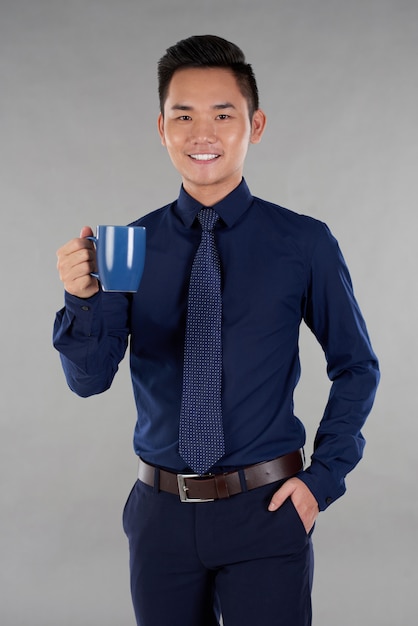Bemannen Sie das indarke blaue formalwear, das gegen grauen Hintergrund mit Marineblau-Tasse Tee steht