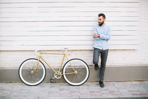 Bemannen Sie das Lehnen auf weißer Wand nahe Fahrrad