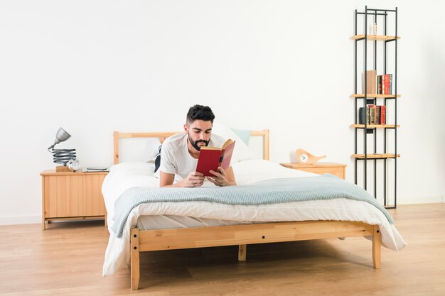 Bemannen Sie das Lügen auf dem Bett, das das Buch im Schlafzimmer liest