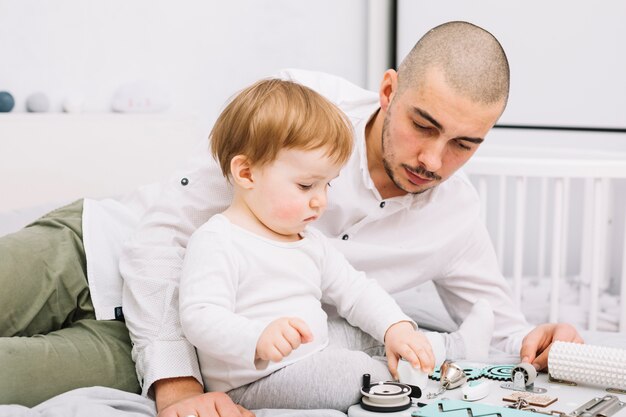 Bemannen Sie das Lügen nahe kleinem Baby mit dem Spielzeug, das auf Bett nahe Krippe sitzt