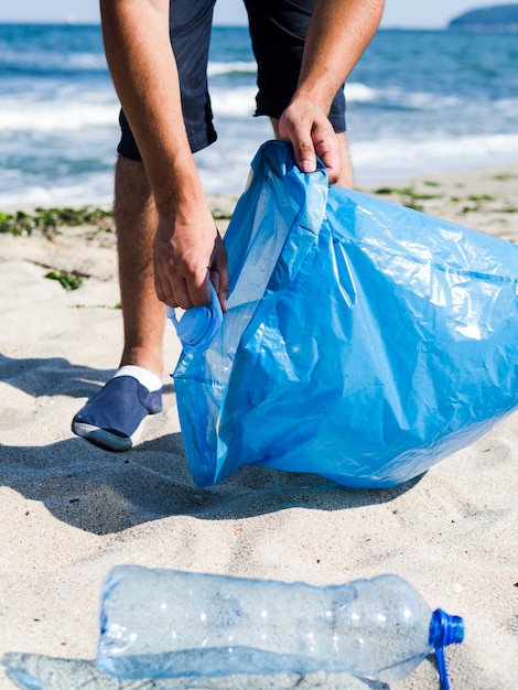 Bemannen Sie das Sammeln des Plastikabfalls vom Strand und das Setzen es in blaue Abfalltaschen für bereiten Sie auf