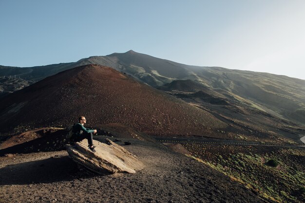 Bemannen Sie das Sitzen auf Felsen und das Genießen der schönen Landschaft des Vulkans Ätna in Sizilien