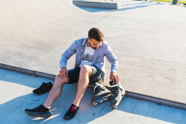 Bemannen Sie das Sitzen im Rochenpark, der sein rollerskate betrachtet