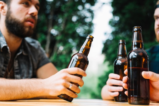 Bemannen Sie das Sitzen mit seinem Freund, der draußen braune Bierflasche hält