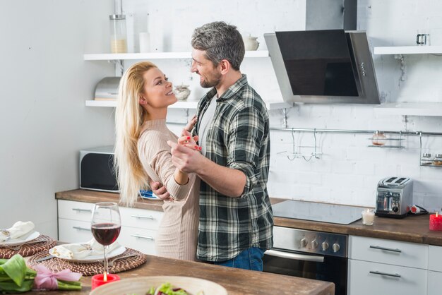 Bemannen Sie das Tanzen mit lächelnder Frau nahe Tabelle in der Küche