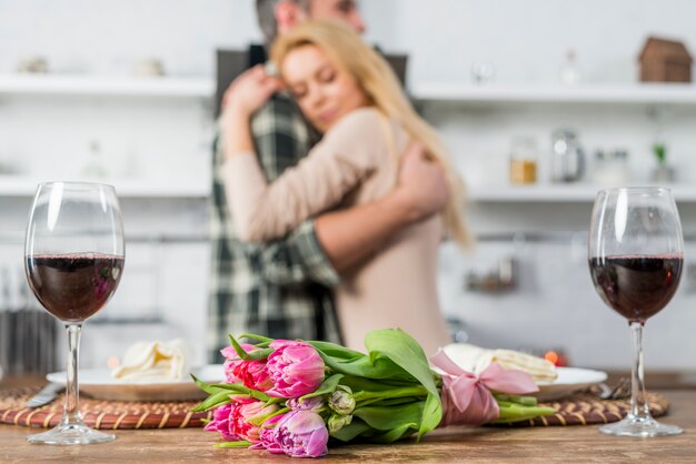 Bemannen Sie das Umarmen mit Frau nahe Tabelle mit Blumen und Gläsern Wein