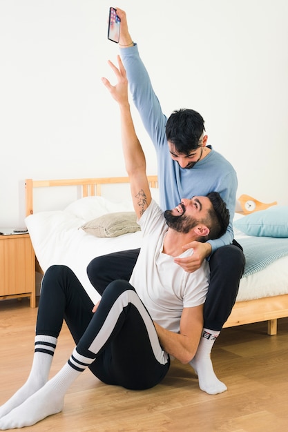 Bemannen Sie das Versuchen, Handy von der Hand seines Freundes zu nehmen, die im Schlafzimmer sitzt