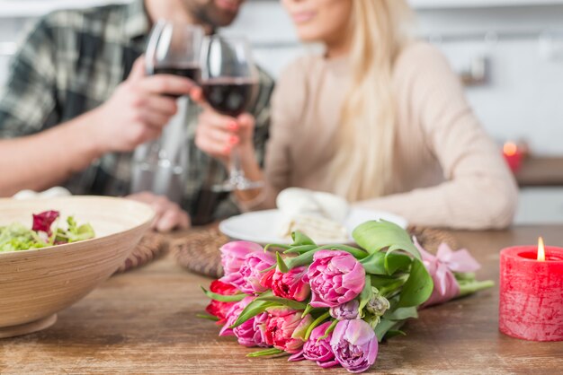 Bemannen Sie klirrende Gläser mit Frau bei Tisch mit Blumen und Schüssel Salat