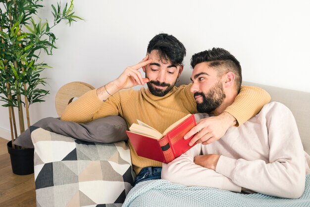 Bemannen Sie seinen Freund betrachten, der zu Hause das Buch liest