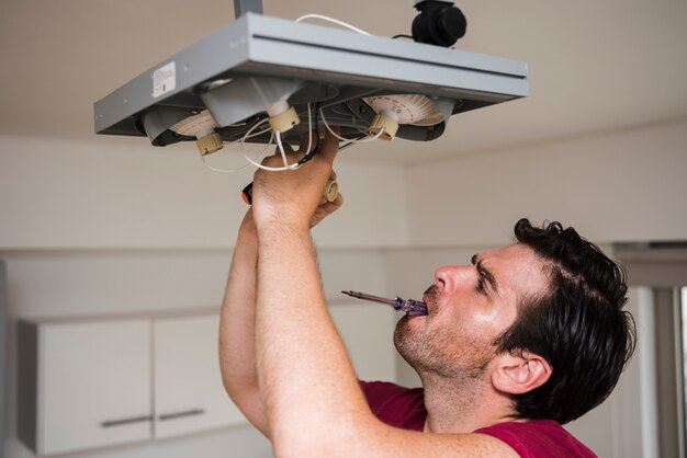 Bemannen Sie tragenden Tester im Mund, während Sie Deckenfokuslicht zu Hause reparieren