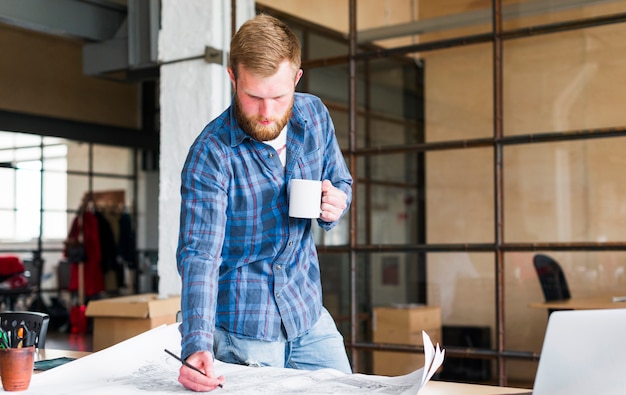 Kostenloses Foto bemannen sie zeichnende blaupause mit dem halten der kaffeetasse in seinem büro