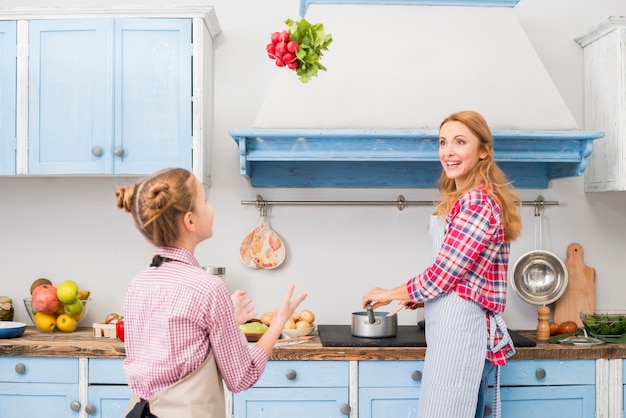 Bemuttern Sie das Kochen des Lebensmittels, das ihren werfenden Rettich der Tochter in einer Luft Küche betrachtet