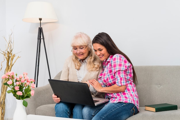 Kostenloses Foto bemuttern sie und ihre junge tochter, die zusammen auf dem sofa sitzt, das laptop betrachtet