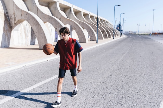 Übender Basketball des Teenagers auf Straße