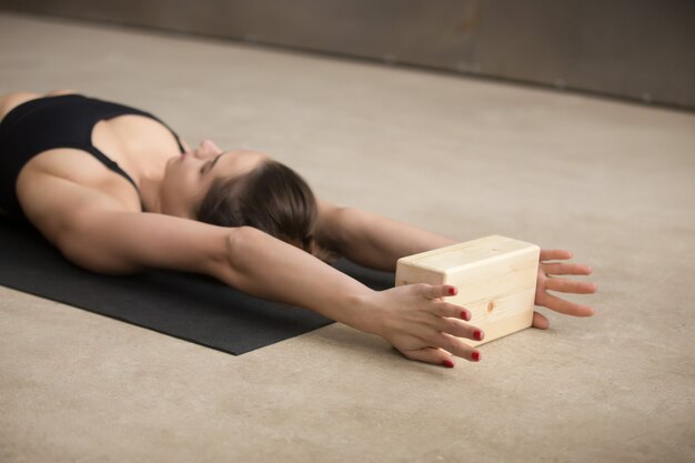 Übendes Iyengar-Yoga der jungen attraktiven Frau unter Verwendung des hölzernen Blocks