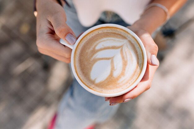 Über dem Rahmen einer Tasse Kaffee in der Hand der Frau draußen in der sonnigen Sommerstraße