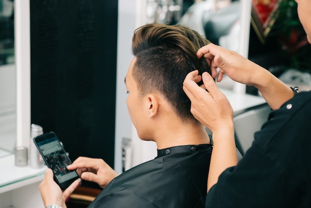 Über der Schulteransicht des nicht erkennbaren geernteten Friseurs, der Wachs auf Haar des Kunden aufträgt