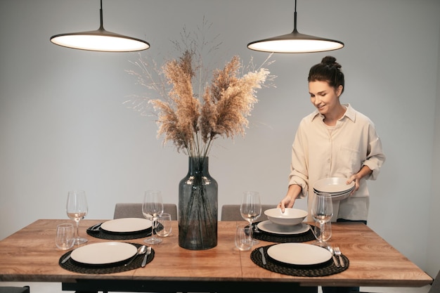 Bereiten Sie sich auf das Abendessen vor. Junge dunkelhaarige Frau, die den Tisch in der Küche bedient