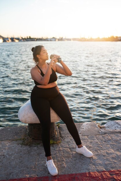 Übergewichtige Frau, die nach dem Training im Freien mit Wasser hydratisiert wird