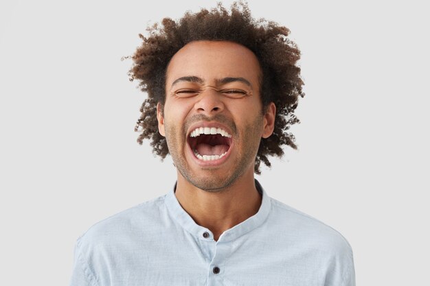 Überglücklicher Mann mit lockiger Frisur, lacht glücklich, hält den Mund weit offen, zeigt weiße Zähne