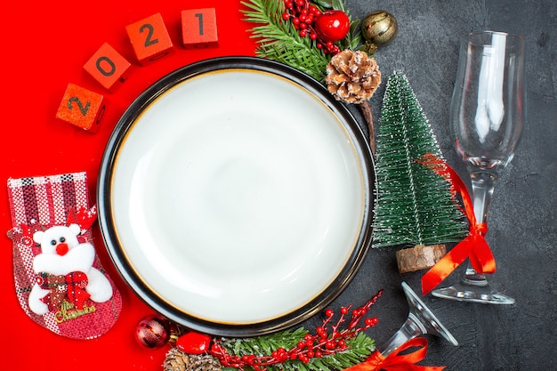 Überkopfansicht der Tellerdekorationszubehör-Tannenzweige-Weihnachtssockenzahlen auf einer roten Serviette und Weihnachtsbaumglasbecher auf dunklem Hintergrund