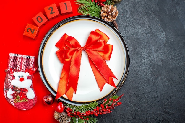 Überkopfansicht des Geschenks mit Band auf Tellerdekorationszubehör Tannenzweigen und Zahlenweihnachtssocke auf einer roten Serviette auf einem schwarzen Hintergrund