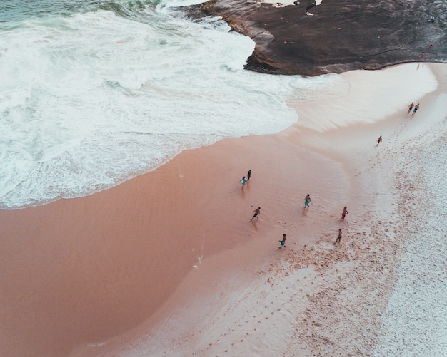 Überkopfaufnahme der Leute, die einen sonnigen Tag an einem Sandstrand nahe schönen Wellen des Meeres genießen