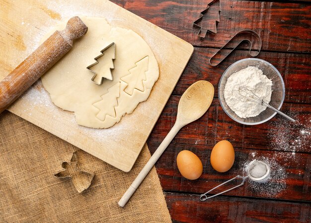 Überkopfaufnahme des rohen Teigs und der Weihnachtsausstecher auf rustikalem Küchentisch