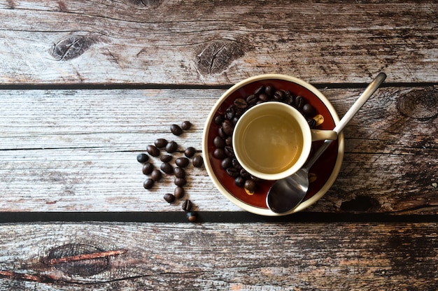 Überkopfaufnahme einer Kaffeetasse in der Nähe von Kaffeebohnen und eines Metalllöffels auf einer Holzoberfläche