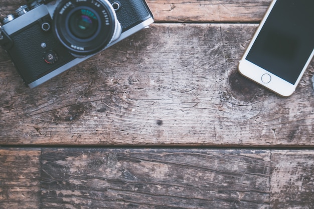 Überkopfaufnahme einer Kamera und eines Smartphones auf einem braunen hölzernen Hintergrund