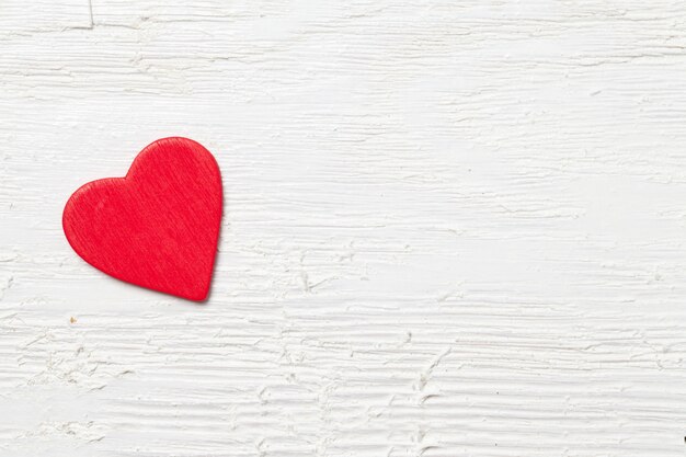 Überkopfaufnahme eines kleinen roten Herzens auf einem weißen hölzernen Hintergrund - romantisches Konzept