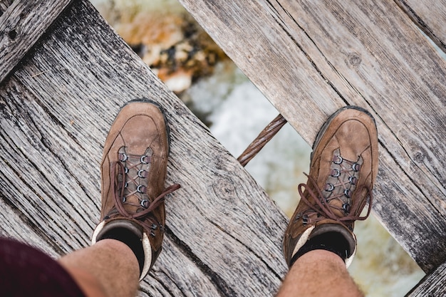 Überkopfaufnahme eines männlichen Fußes, der auf einer Holzbrücke steht, die Wanderschuhe trägt