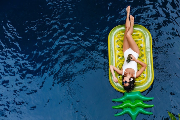 Überkopfporträt des gewinnenden Mädchens, das im Pool schwimmt. Wunderschöne kaukasische gebräunte Frau, die Wochenende im Sommerresort verbringt.