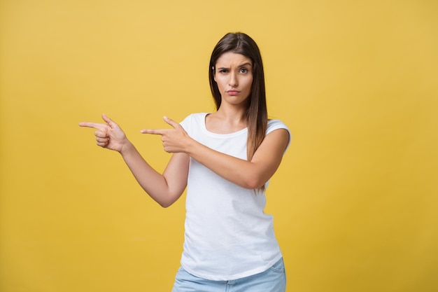 Überraschen Sie die junge Frau, die mit ihrem Finger auf eine Seite zeigt, während sie ihren Mund vor einem gelben Hintergrund öffnet