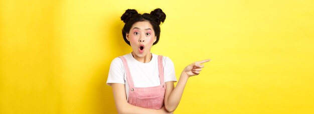 Überrascht asiatische Teenager-Mädchen suchen beeindruckt sagen wow und zeigen mit dem Finger nach links stehen mit Glamour m