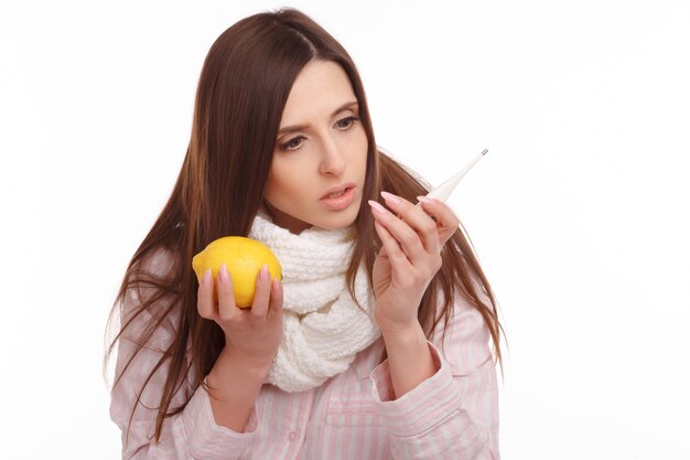 Überrascht Frau mit Zitrone in der Hand und schaut auf einen Thermometer