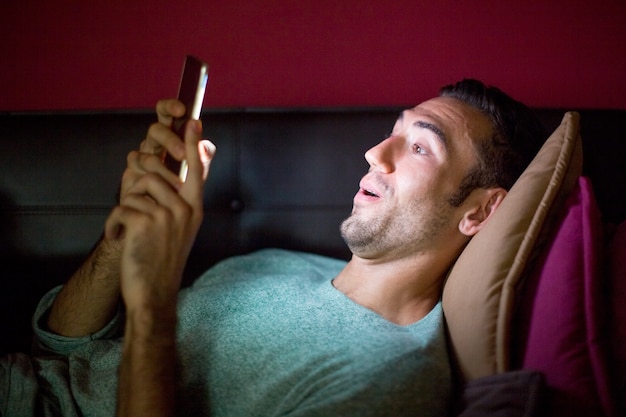 Überrascht Mann mit Smartphone auf Sofa bei Nacht