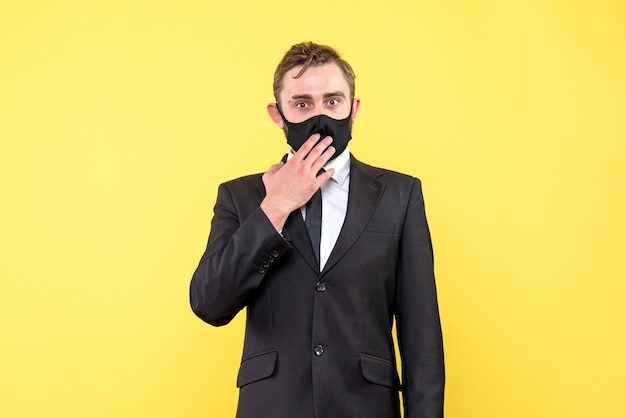Überrascht steht junger Mann in einer Schutzmaske mit Anzug und Krawatte auf gelb