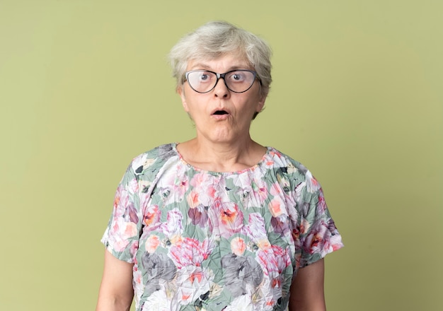 Überraschte ältere Frau in optischen Gläsern sieht auf olivgrüner Wand isoliert aus