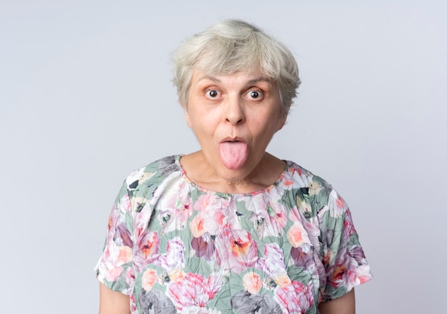 Überraschte ältere Frau ragt Zunge heraus, die auf weißer Wand isoliert wird