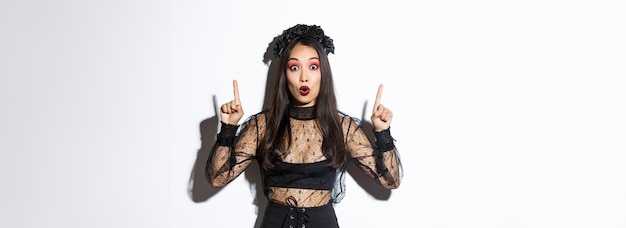 Überraschte asiatische Frau im Halloween-Kostüm, die erstaunliches Promo-Angebot für Halloween-Zeigefinger zeigt
