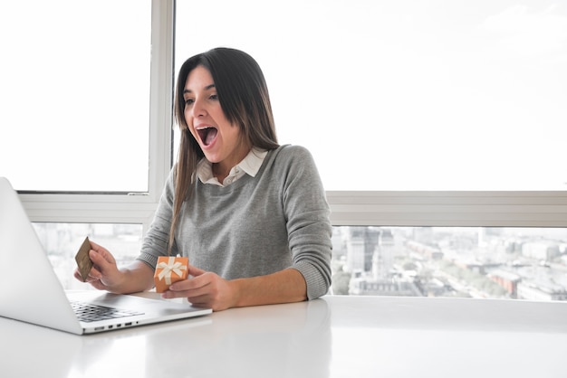 Überraschte Frau, die bei Tisch mit Laptop sitzt