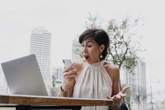 Überraschte Frau, die ein Telefon auf städtischem Hintergrund hält