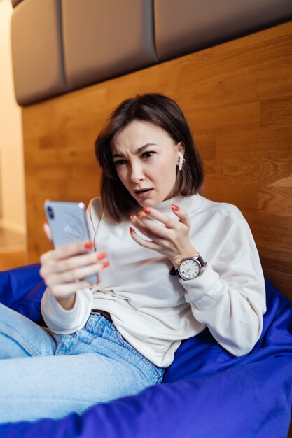 Überraschte Frau sitzt in einem hellvioletten Taschenstuhl und benutzt ihr Telefon, um mit ihren Freunden eine SMS zu schreiben