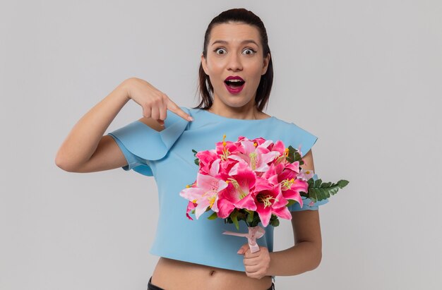 Überraschte hübsche junge Frau, die einen Blumenstrauß hält und zeigt