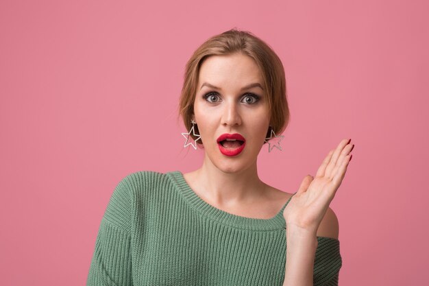 Überraschte junge attraktive Frau mit schockiertem Gesichtsausdruck, offenem Mund, Hände hoch, lustiges Gefühl, rote Lippen, Modell, das im Studio aufwirft, isoliert, rosa Hintergrund, Blick in die Kamera,