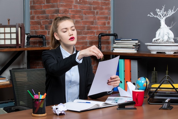 Überraschte junge Dame, die an einem Tisch sitzt und ihre Notizen im Notizbuch im Büro liest