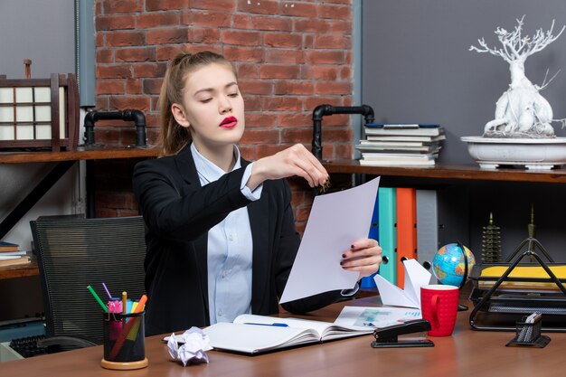 Überraschte junge Dame, die an einem Tisch sitzt und ihre Notizen im Notizbuch im Büro liest